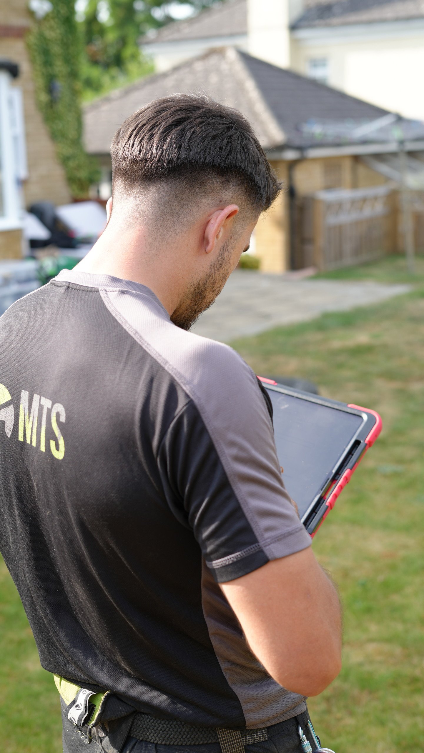 Maidstone Tree Surgeons team member checking job details on a tablet in a garden
